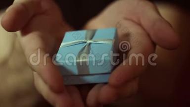 男人在一个蓝色的盒子里拿出一份礼物。 一个年轻人的手在一个蓝色`小盒子里捧着新年礼物。 假期的礼物。